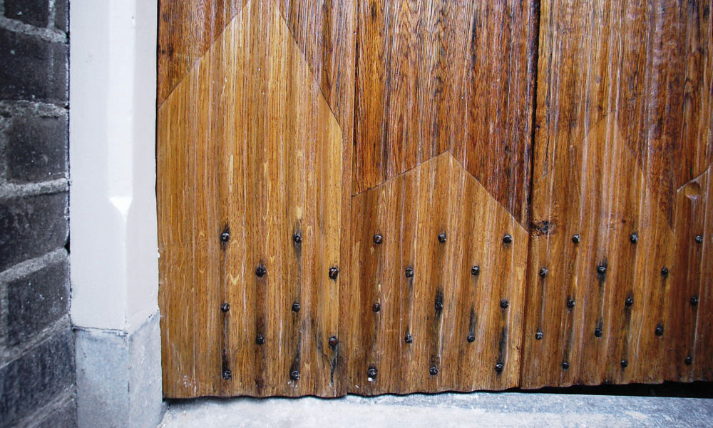 De ingerotte onderkant van een ‘gecanneleerde’ eiken buitendeur is hersteld door inschieten van nieuwe delen in dezelfde houtsoort en detaillering.